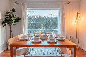 Un comedor con una mesa dispuesta para seis personas, una planta en maceta y vistas a un bosque a través de una ventana.