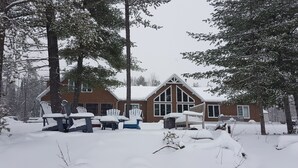 Un chalet enneigé, doté d’une grande cheminée, d’une terrasse en bois et de meubles recouverts de neige.