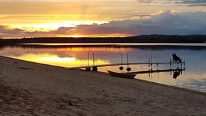 Une plage avec une jetée en bois s’avançant dans des eaux calmes, un ciel dégagé et un coucher de soleil.
