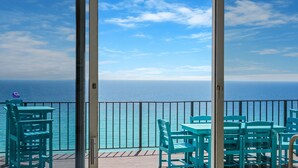 Een balkon met turquoise stoelen en tafels met uitzicht op zee.