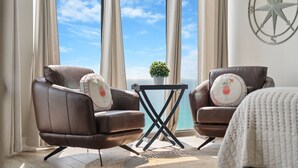 Een kamer met twee leren fauteuils, een tafeltje, een plant in pot en uitzicht op zee.
