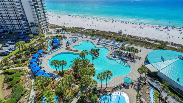 Een resort met een groot zwembad, strand en een parkeerplaats.