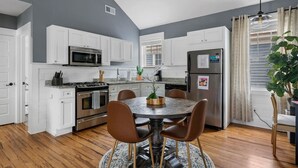 A modern kitchen with white cabinets, stainless steel appliances, and a round dining table with chairs. - Spring St - Downtown - Walk Everywhere! (Charleston)