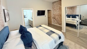 Un dormitorio con cama, ventilador de techo, televisor, pared de ladrillo y puerta corredera.