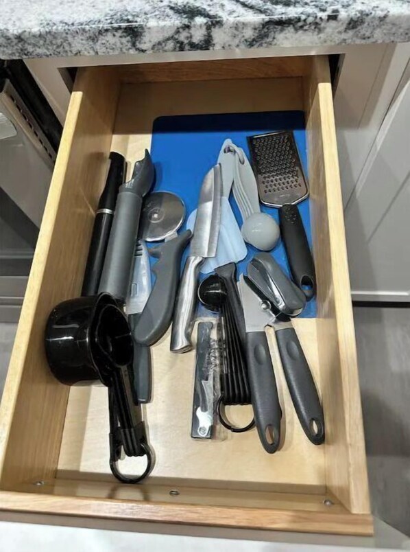 A drawer with various kitchen utensils including a grater, a knife, and a can opener. - Rustic Charm 4BDRM Home| STL Developers (St. Louis)