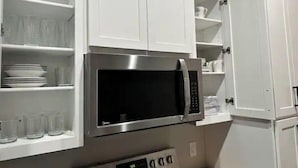 Una cocina con armarios blancos, un microondas de acero inoxidable y un horno empotrado.
