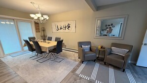 Un salon moderne avec un coin repas, agrémenté d’un lustre, d’un grand tableau et d’un ensemble de canapés.