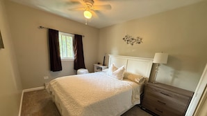 Une chambre à coucher comprenant un lit, une table de chevet, une commode et un ventilateur de plafond.