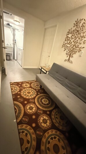 A living room with a sofa, patterned rug, and a wall-mounted tree decoration. - Convenient location and clean home (Golden)