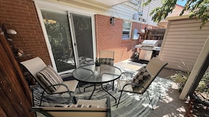 Une terrasse avec une table ronde en verre, quatre chaises et un barbecue.