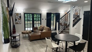 Un salon moderne avec un canapé marron, une table de salle à manger ronde entourée de chaises et un escalier menant à un niveau supérieur.