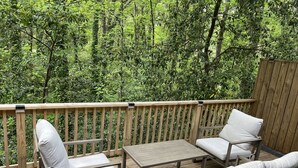 Une terrasse en bois avec une table et quatre chaises, entourée d’une végétation luxuriante.