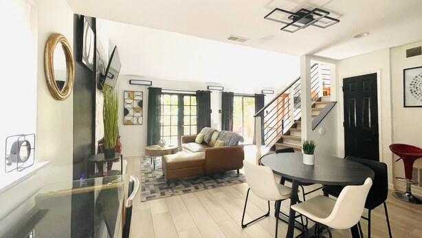 Un salon moderne comprenant un canapé, une table à manger avec des chaises, un escalier et un coin cuisine avec un réfrigérateur et un évier.