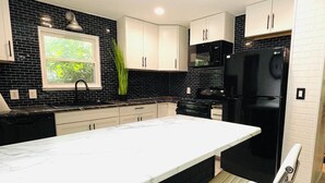 Une cuisine moderne dotée d’un grand îlot central, de meubles de rangement noirs et blancs et d’un réfrigérateur noir.