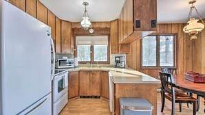 Una cocina con paneles de madera, un refrigerador blanco, un microondas, una cafetera y una mesa de comedor con sillas.