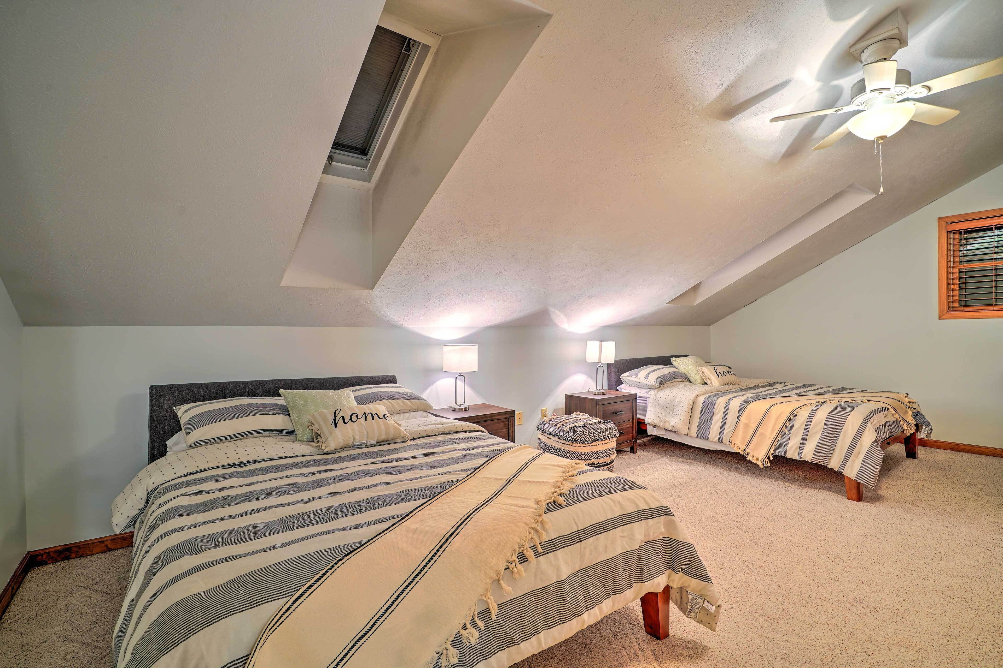 A bedroom with two beds, a ceiling fan, and a skylight.