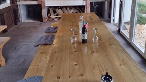 Un espacio comedor rústico al aire libre con horno de ladrillo, mesa de madera y asientos.