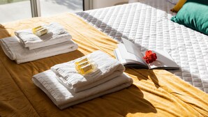 A neatly made bed with a yellow blanket, white towels, and a book with a red flower. - Santa Bárbara Sunset 27 C (Santa Bárbara)