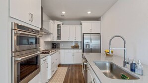 Una cocina moderna con electrodomésticos de acero inoxidable, armarios blancos y un lavamanos de acero inoxidable.