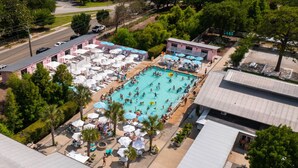 Vista aérea de un resort con una gran piscina rodeada de tumbonas y sombrillas, un estacionamiento y un edificio con techo rojo.