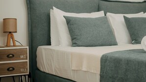 A bed with a green headboard, white bedding, and multiple pillows. There is a bedside table with a lamp and two drawers labeled "No.1" and "No.2". A framed picture hangs on the wall above the bed.