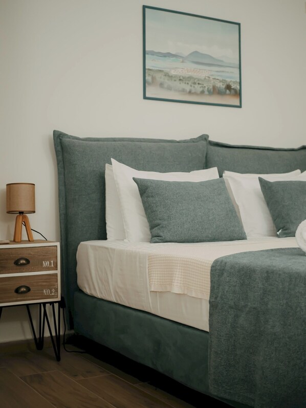 A bed with a green headboard, white bedding, and multiple pillows. There is a bedside table with a lamp and two drawers labeled "No.1" and "No.2". A framed picture hangs on the wall above the bed.