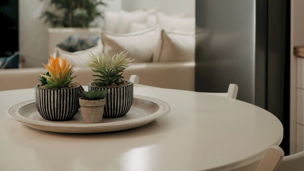 A modern kitchen with a white table, three striped planters with succulents, a stainless steel refrigerator, and a potted plant in the background.