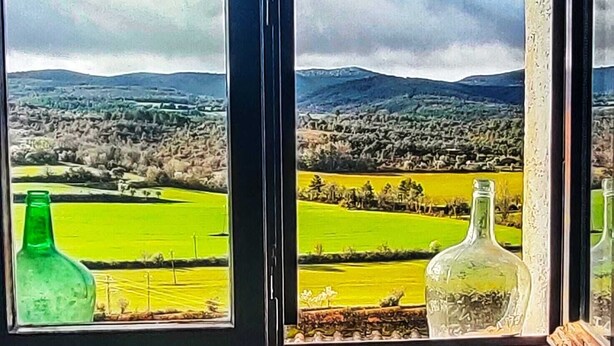 A window with a view of a green field and distant hills. - Rural house in a small town. (Aler)