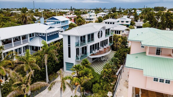 A coastal residential area with modern houses featuring large windows and balconies, surrounded by lush greenery and palm trees.