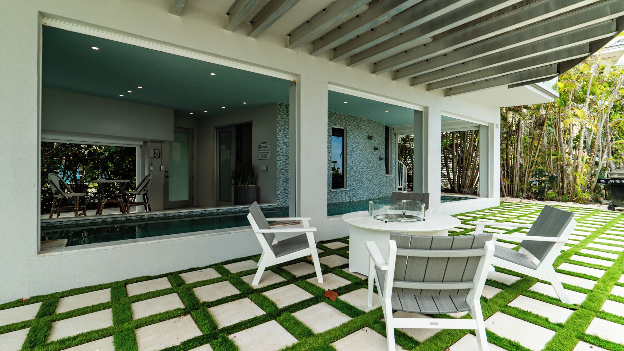 A modern outdoor patio with a pool, seating area, and a view of the surrounding greenery.