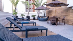 Un área de estar al aire libre con sillones, una mesa redonda y sombrillas.