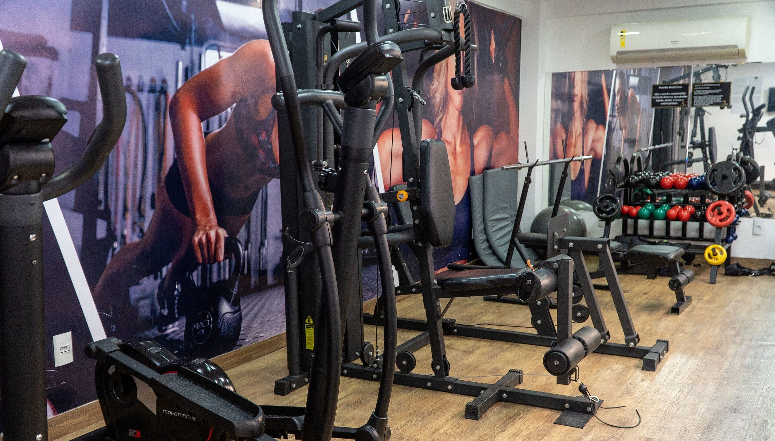Un gimnasio con equipo de ejercicio, una banca de pesas y una pared con un cartel.