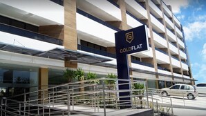 Entrada de hotel con un letrero que dice 'GOLDFLAT', una escalera y un estacionamiento con coches.