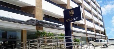 A hotel entrance with a sign labeled 'GOLDFLAT,' a staircase, and a parking area with cars.