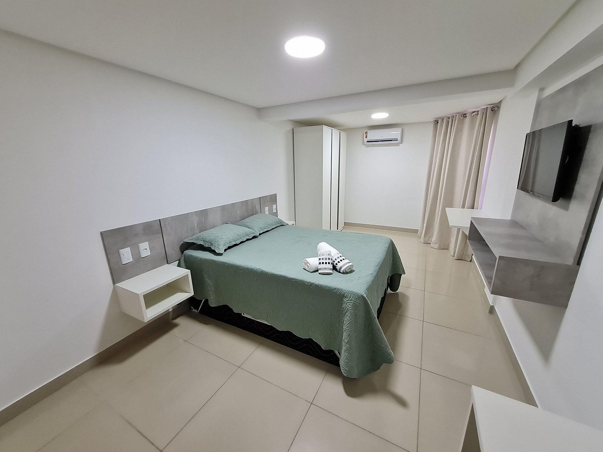 Een slaapkamer met een bed, nachtkastje, ingebouwde plank, airconditioning en een televisie.