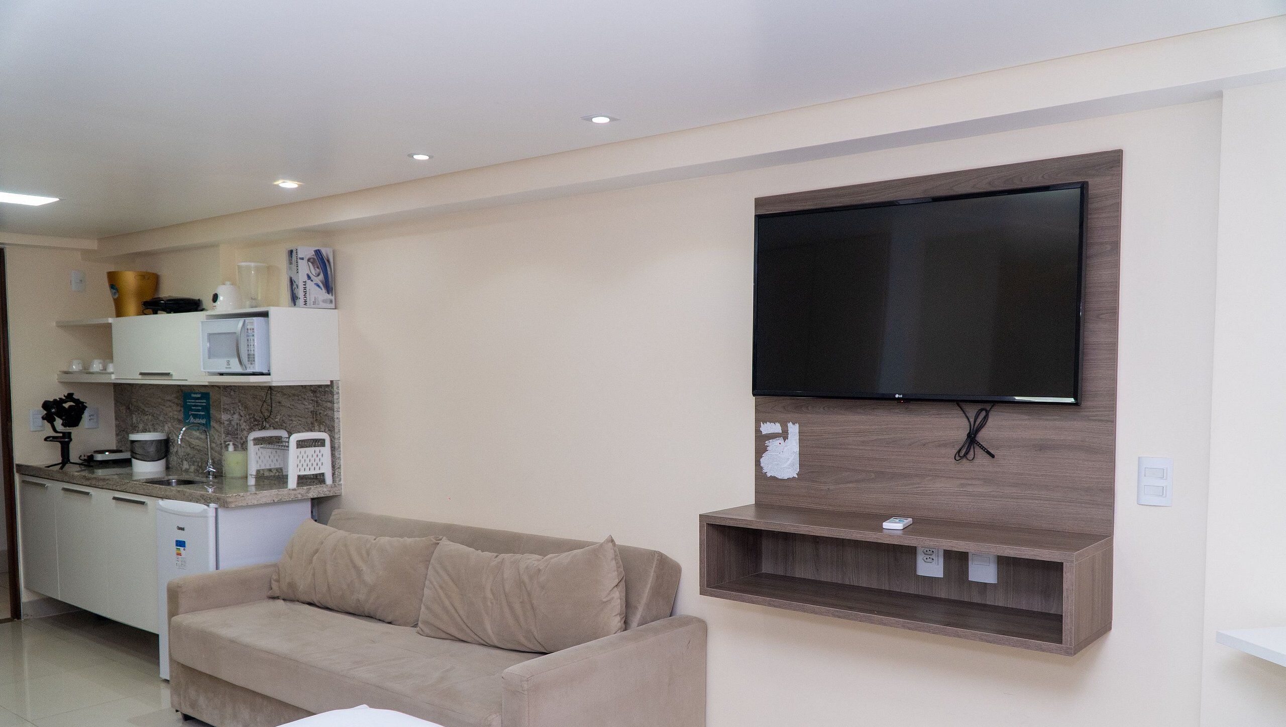 A living room with a flat-screen TV, a sofa, a kitchen area with a microwave, and a coffee maker.