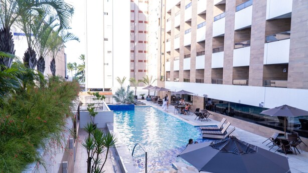 Un hotel con piscina, mobiliario exterior y palmeras.
