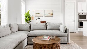 Un salon moderne avec un canapé d’angle gris, une table basse en bois sur laquelle sont posés des livres, une plante et deux œuvres d’art encadrées accrochées au mur.