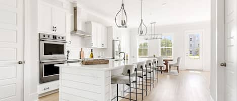 A modern kitchen with white cabinetry, a central island with bar stools, stainless steel appliances, and pendant lighting.