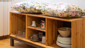 A wooden cabinet with floral cushions on top, containing various kitchenware including bowls, plates, and cups. - Appartamento Ariento (Florence)