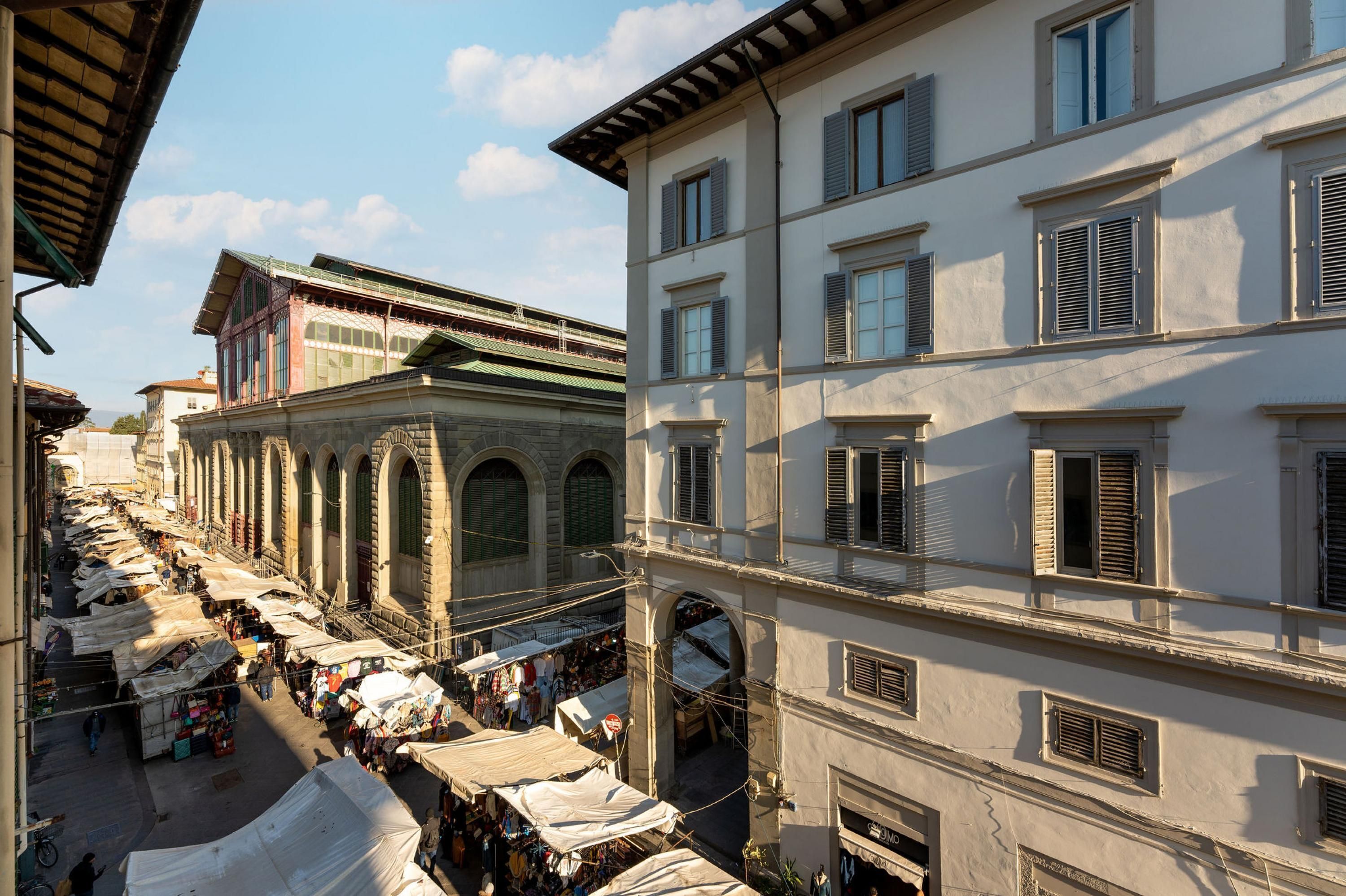 A street market with stalls and a building with arched windows and shutters.