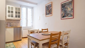 A dining area with a wooden table and chairs, a kitchen in the background, and two framed artworks on the wall. - Appartamento Ariento (Florence)