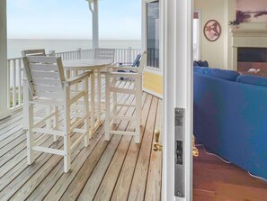 A wooden deck with white chairs and a table, a blue sofa, and a view of the ocean. - Turtle Watch 4 Bedroom Home by RedAwning (Panama City Beach)