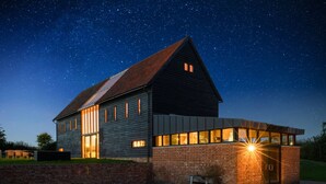 A modern two-story house with large windows and a sloped roof, set against a starry night sky. - Grand Suffolk Barn Conversion (Suffolk)