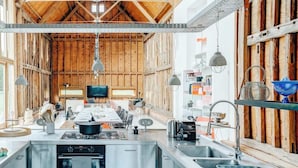 A modern kitchen with a central island, stainless steel appliances, and wooden beams. - Grand Suffolk Barn Conversion (Suffolk)