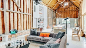 A spacious loft with exposed wooden beams, a cozy seating area with a sofa and chairs, a dining table, and a kitchen area. - Grand Suffolk Barn Conversion (Suffolk)