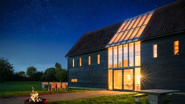 A rustic wooden house with large windows and a fire pit in the yard. - Grand Suffolk Barn Conversion (Suffolk)