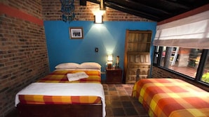 Une chambre avec deux lits, un mur en briques, un mur d’accent bleu, une armoire en bois et une fenêtre donnant sur un beau paysage.