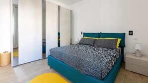 Ein modernes Schlafzimmer mit einem türkisblauen Bett, einem gelben Sessel und einem weißen Nachttisch.