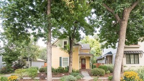 Une maison à deux étages dotée d’un porche à l’avant, entourée d’arbres matures et agrémentée d’un aménagement paysager soigné.